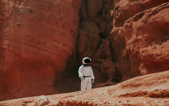 An astronaut in a space suit standing next to rock faces in a desert.